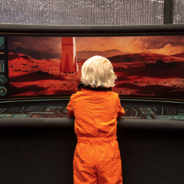 Young boy dressed in astronaut suit pushing buttons on a control panel in a pretend spacecraft